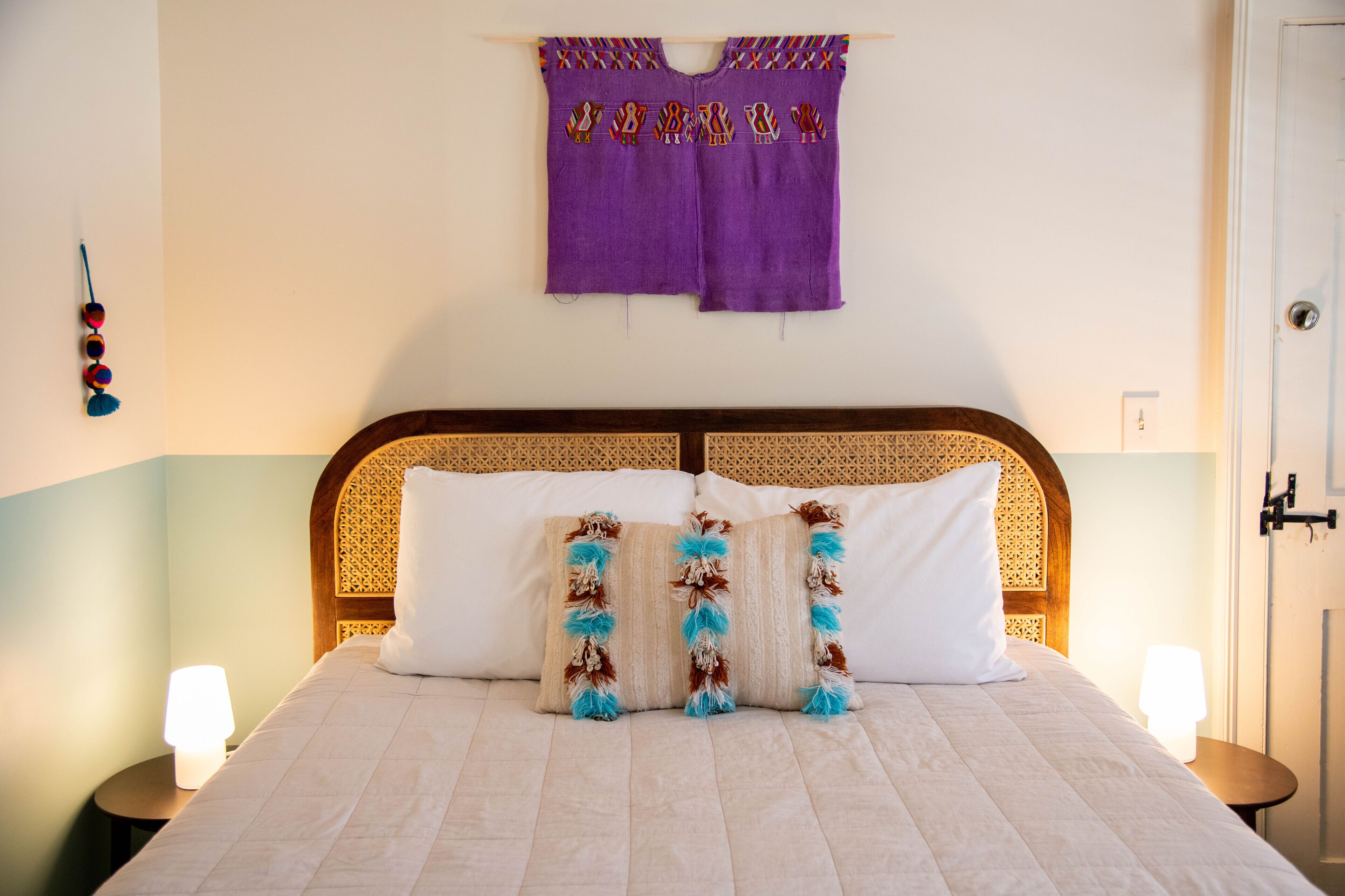 A neatly made bed with white linens and decorative pillows, a wooden headboard, and a wall-mounted curtain.