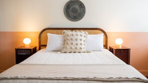 A neatly made bed with a white duvet, two bedside tables with lamps, and a decorative plate on the wall. - The Vesper  (Woodstock)
