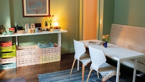 A dining area with a white table, two white chairs, a small vase with flowers, and a framed artwork on the wall. - The Vesper  (Woodstock)