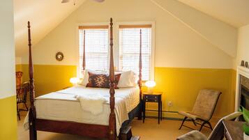 Een slaapkamer met een hemelbed, een nachtkastje, een stoel en een open haard.