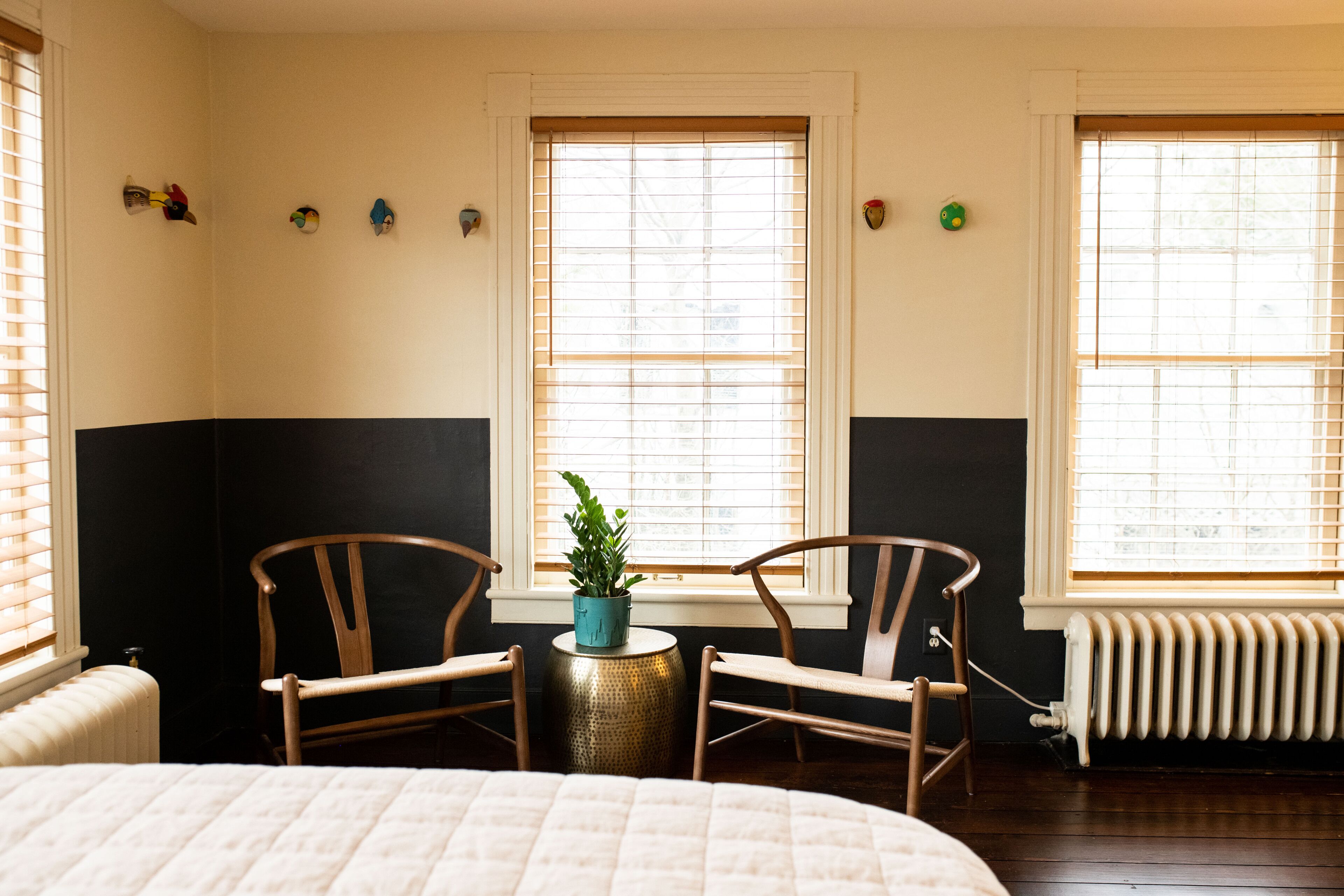 A room with a bed, two wooden chairs, a small table with a potted plant, and a radiator.