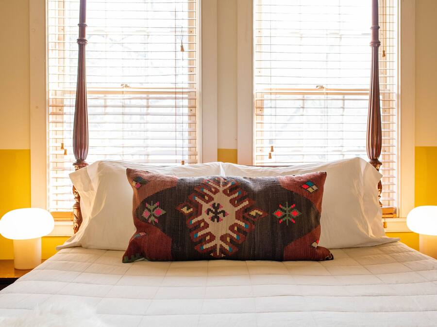 A bed with a patterned pillow, two bedside lamps, and a window with blinds.