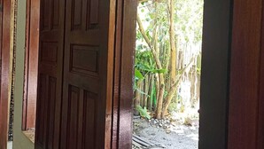 Una puerta de madera con un pestillo metálico, que da a un espacio exterior con suelo de baldosas y un paseo cubierto.