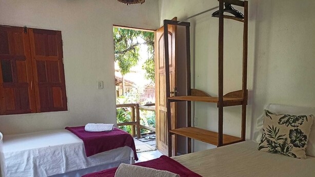 Una habitación con dos camas, una con colcha roja y la otra con colcha blanca. A la derecha, hay una estantería de madera con un perchero.