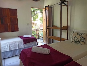 A room with two beds, one with a red bedspread and the other with a white bedspread. There is a wooden shelf unit with a hanging rack on the right side.