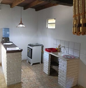 A compact kitchen with a water dispenser, a stove, a sink, and a hanging light fixture.