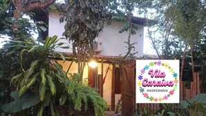 Un jardín con un letrero de Vila Carava HOSPEDARIA, rodeado de exuberante follaje y una estructura de madera.