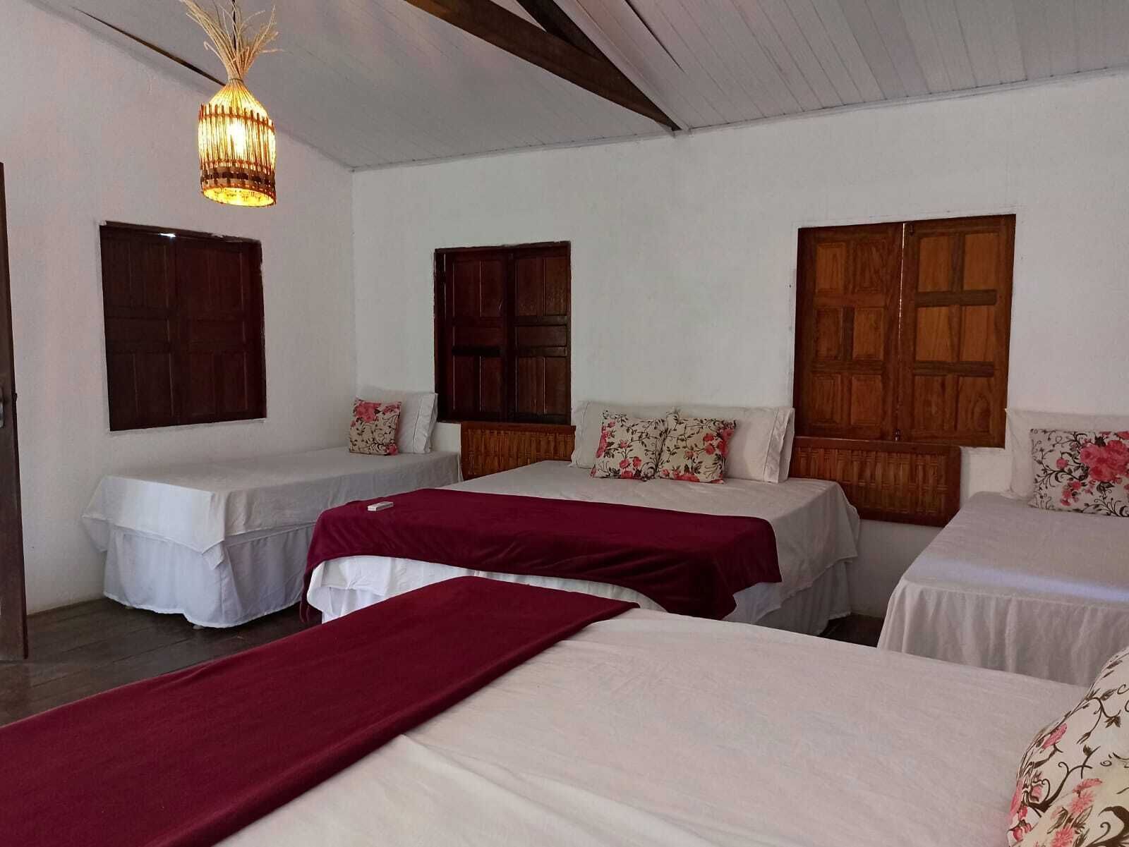 Una habitación con tres camas, cada una con un cubrecolchón blanco y un corredor rojo. Hay puertas de madera y una lámpara colgante.