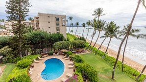A pool surrounded by lounge chairs, palm trees, and a building with a view of the beach. - Kealia Unit 206 Oceanfront Views Kihei Condo AC in bedroom and living room (Kihei)