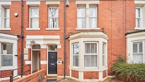 A red brick terraced house with a bay window, a black front door, and a small front garden.