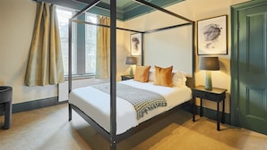 A four-poster bed with a white and black bedspread, two bedside tables with lamps, and a window with curtains.