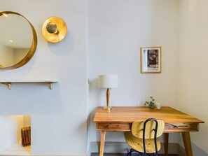 Ein Zimmer mit einem Holztisch, einem Stuhl, einer Lampe, einem Spiegel und einem gerahmten Bild an der Wand.