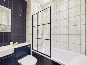 A modern bathroom with a bathtub, a toilet, and a shower enclosed by a glass partition. - Bright & Stylish Home by Abbey Road Studios (Greater London)