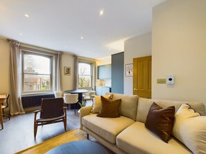 Ein Wohnzimmer mit einer Couch, Sesseln, einem Esstisch und einem fenster mit Vorhängen.