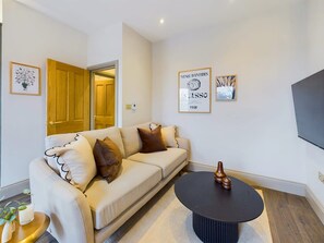 A living room with a beige sofa, a round coffee table, and a flat-screen TV mounted on the wall. - Bright & Stylish Home by Abbey Road Studios (Greater London)