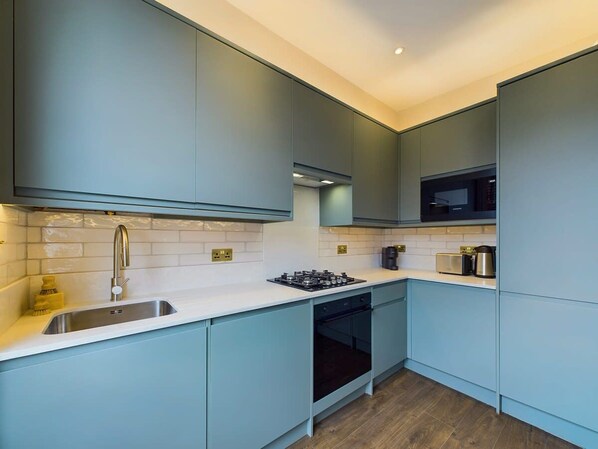 A modern kitchen with light blue cabinets, a stainless steel sink, a built-in oven, and a microwave. - Bright & Stylish Home by Abbey Road Studios (Greater London)