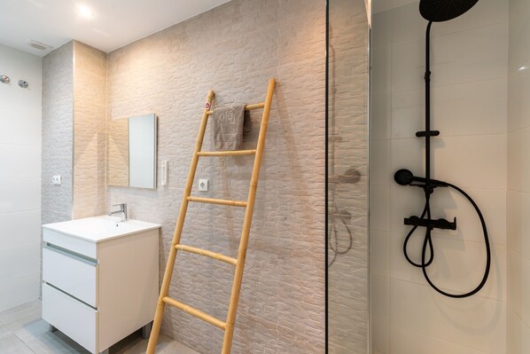 A bathroom with a white sink, a mirror, a shower with a black hose, and a wooden ladder leaning against the wall.