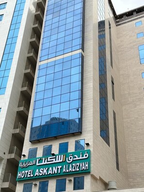 A modern building with a large glass facade and a sign for Hotel Askant Alaziya. - Askant Al Azizyia Hotel (Makkah)