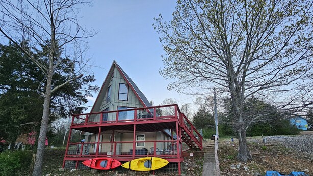 Une maison à deux étages, avec une façade rouge et un balcon. On peut voir des kayaks et un canoë bleu près de la maison.
