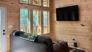 Interior acogedor de una cabaña con techo de madera, ventanas amplias, televisor de pantalla plana y una zona de estar confortable.