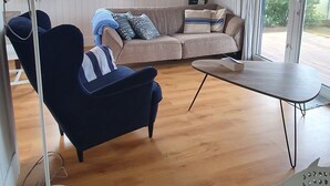 A room with a blue sofa, a wooden coffee table, a lamp, and a view through large windows.