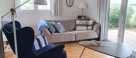 A room with a blue sofa, a wooden coffee table, a lamp, and a view through large windows.