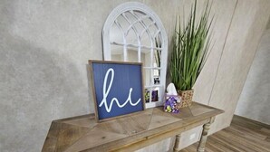Una panca di legno, un cartello blu, uno specchio ad arco bianco e una pianta in vaso.