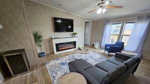 Un soggiorno moderno con camino, televisore, ventilatore a soffitto e vista sull'esterno.
