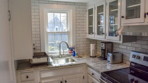 A kitchen with white cabinets, a stainless steel range hood, a built-in oven, a window with a view, and a countertop with a coffee maker and toaster. - Adorable two bedroom sleeping 6 in West Dennis, .6 miles to the beach! (West Dennis)