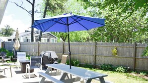 A backyard patio with picnic tables and a blue umbrella. - Adorable two bedroom sleeping 6 in West Dennis, .6 miles to the beach! (West Dennis)