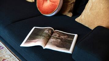 Un libro abierto sobre un sofá azul oscuro con un cojín y un objeto redondo al fondo.