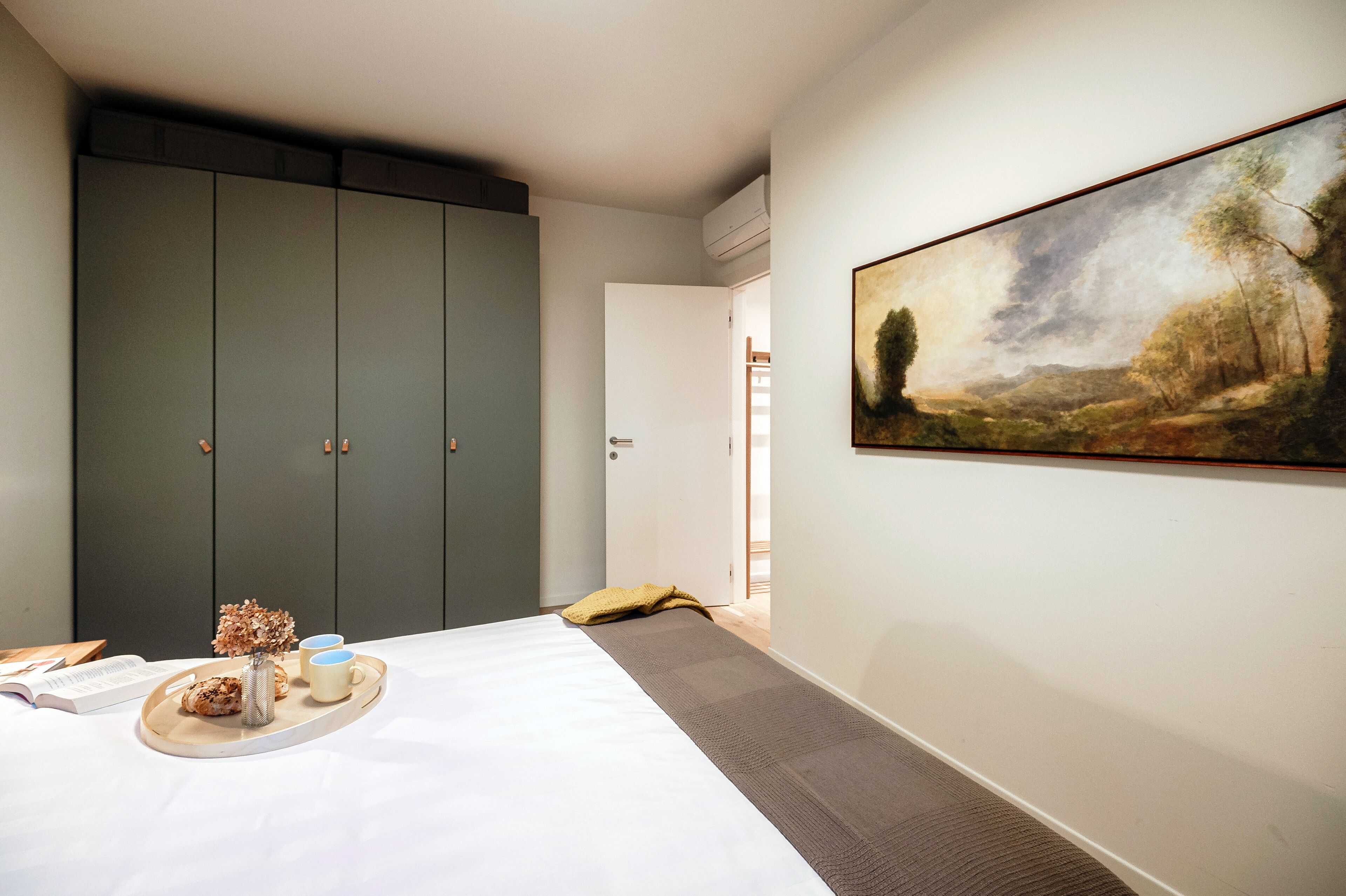 A bedroom with a bed, a tray with snacks, a painting on the wall, and a wardrobe.