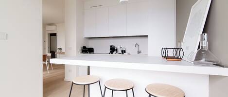 Una cocina moderna con encimera blanca, tres taburetes y una lámpara colgante.