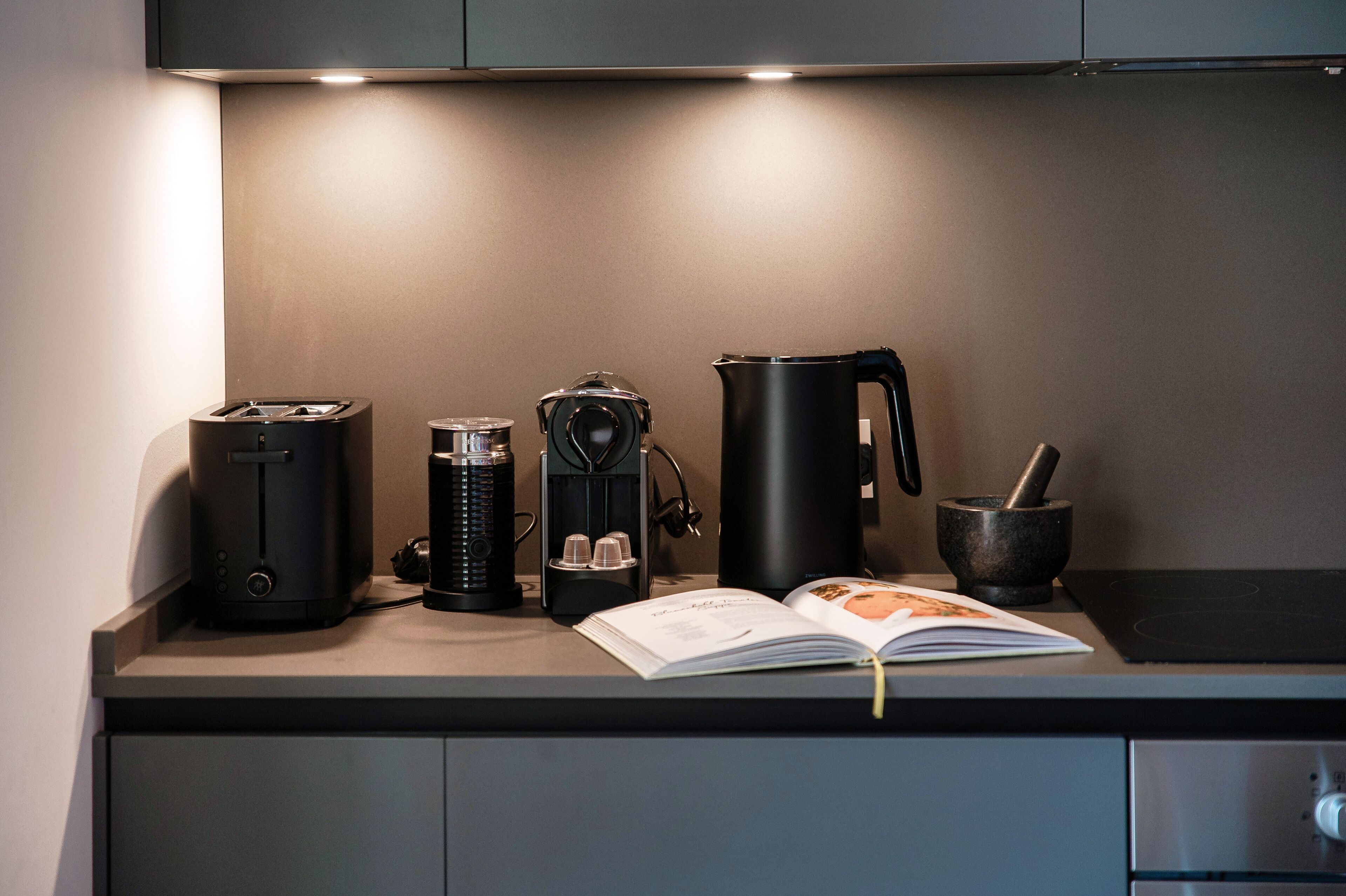 Un comptoir de cuisine avec une machine à café, une bouilloire, un livre et une cuisinière.