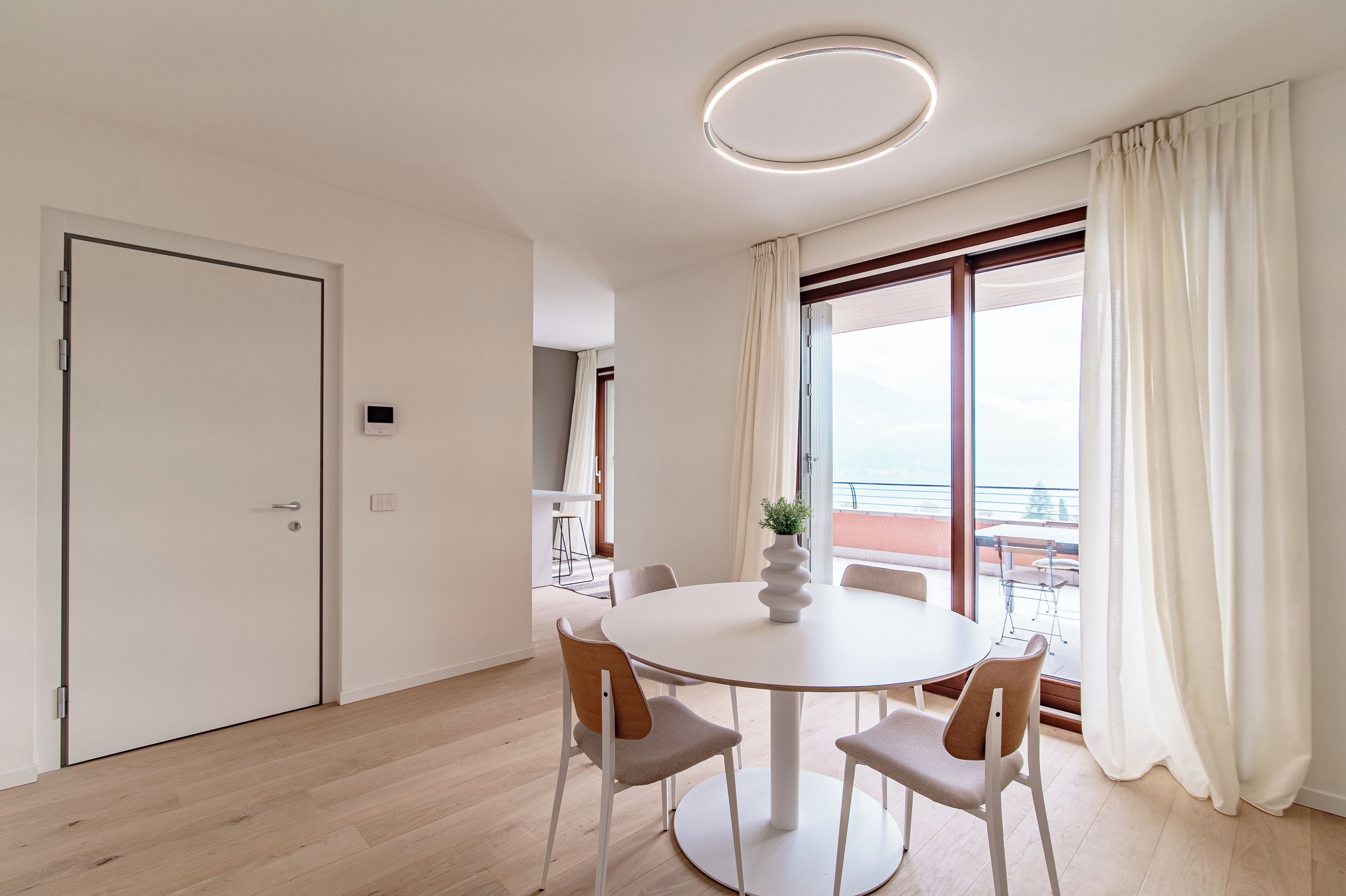 Un coin repas moderne avec une table ronde, quatre chaises, une plante en pot et une grande fenêtre avec des rideaux.