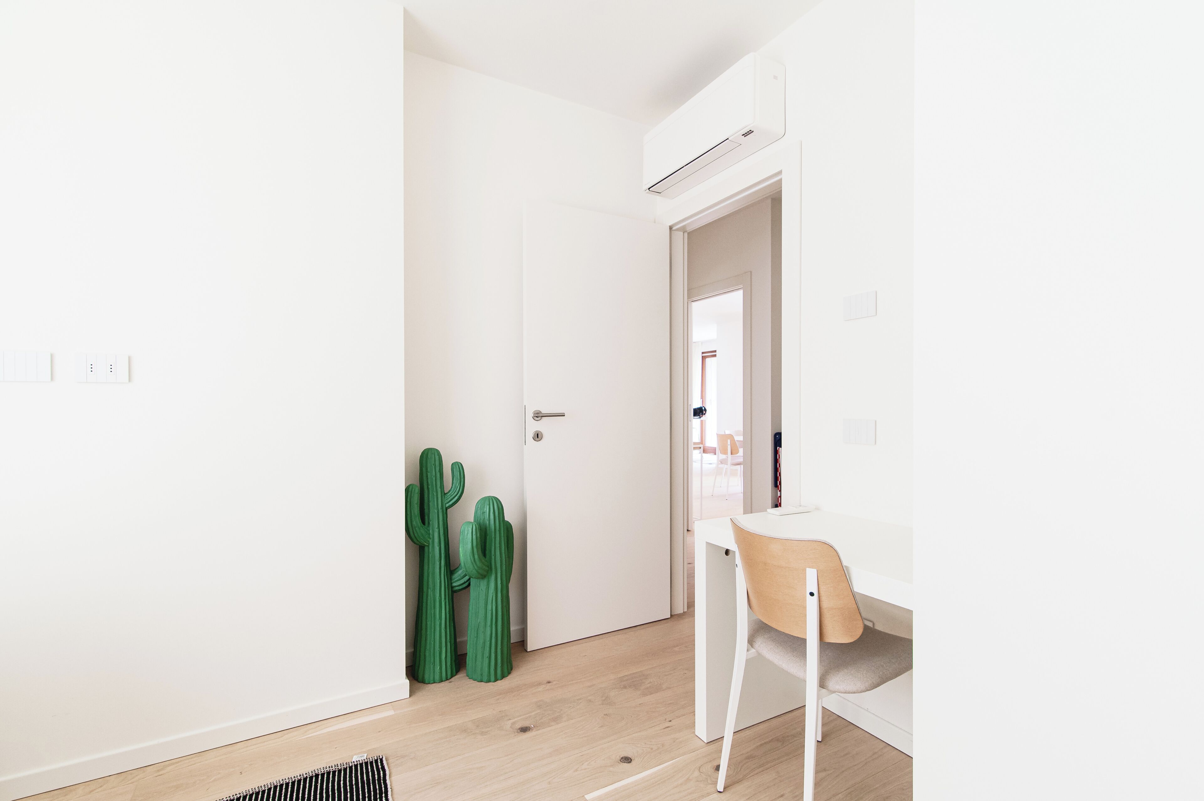 A minimalist room with a white door, a small table with a chair, and two green cactus plants.