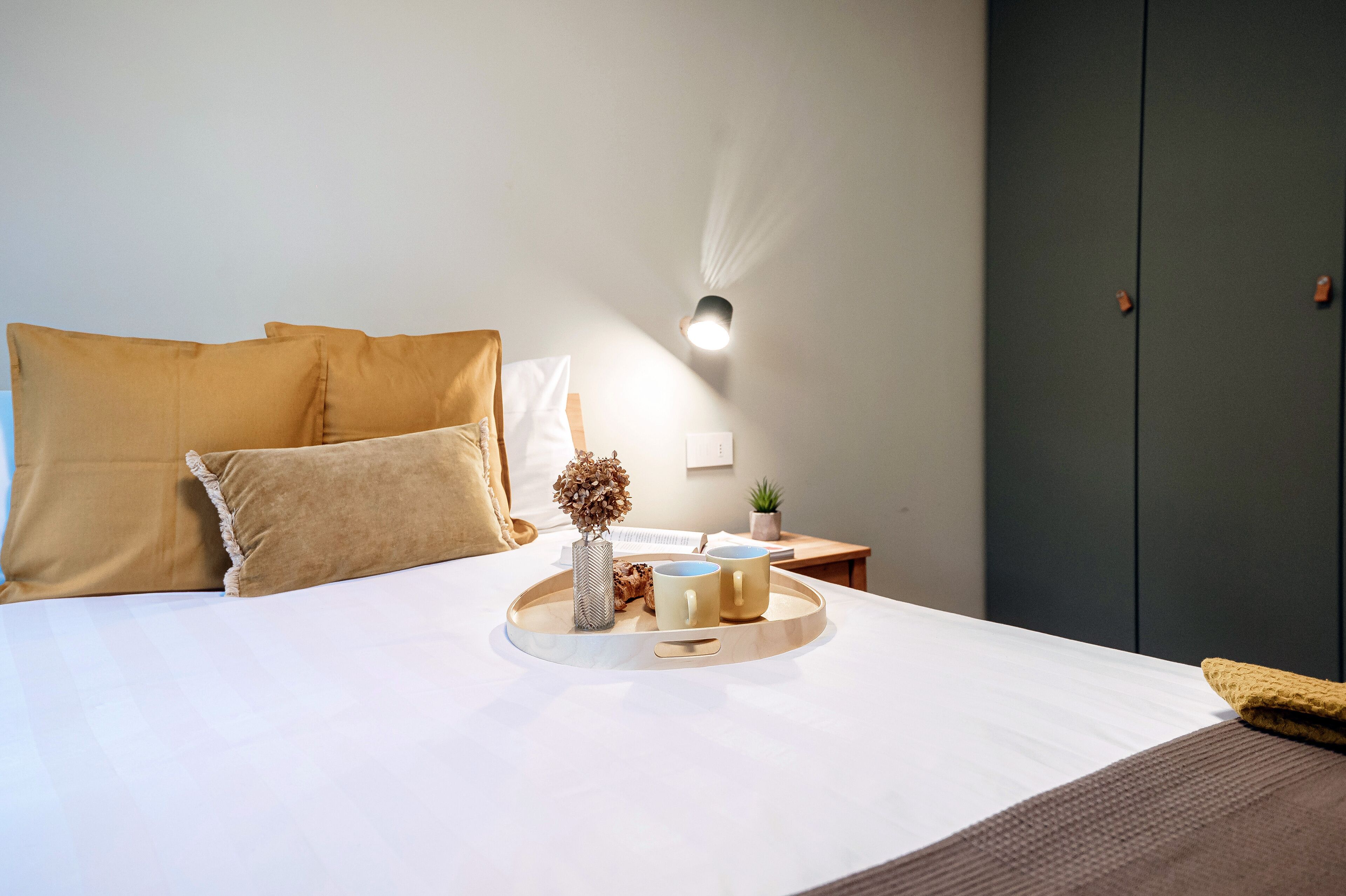 A neatly made bed with a tray of items, including a vase and two mugs, on a white bedspread.