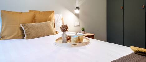 Cama arrumada com uma bandeja de objetos, incluindo um vaso e duas canecas, sobre um lençol de cama branco.