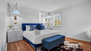 A bedroom with a bed, bedside tables, a blue bench, a cowhide rug, and a window with blinds.