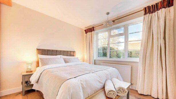 A bedroom with a bed, bedside table, lamp, window, and curtains.