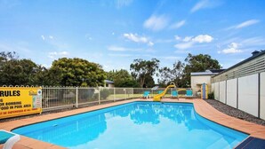 A swimming pool with a fenced area, a slide, and lounge chairs.