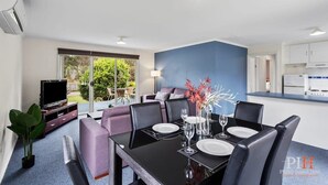 A modern living room with a dining area, a TV, and a kitchen in the background.