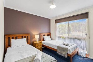 Une chambre d’hôtel avec deux lits, une tête de lit en bois, une table de chevet avec une lampe et une grande fenêtre donnant sur un paysage verdoyant.