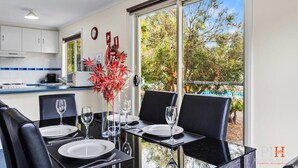 Une cuisine moderne avec des meubles blancs, un pare-feu bleu à rayures et un coin repas avec des chaises noires et une table en verre.