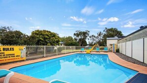A swimming pool with a fenced area, a slide, and lounge chairs.