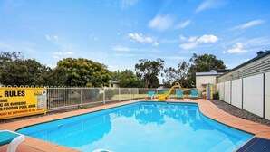 A swimming pool with a fenced area, a slide, and lounge chairs.