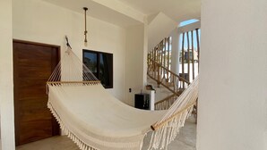 A spacious room with a hammock, a wooden door, and a staircase with a railing. - Casa Hamaca Nayarit (Chacala)