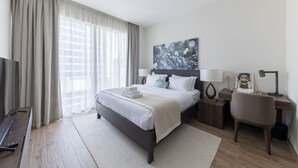 A modern hotel room with a large bed, a desk, a chair, and a TV.