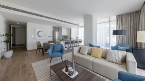 A modern living room with a sofa, armchairs, a coffee table, and a dining area with chairs and a kitchen in the background.