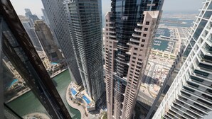 A high-rise building with a modern architectural design, featuring a prominent glass facade and a view of a marina and water body below.
